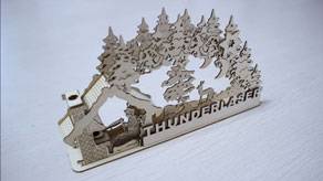 Cutout display of a house and trees with the ThunderLaser logo